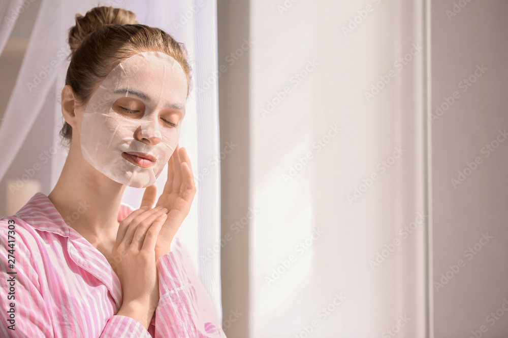 Young woman with sheet facial mask at home