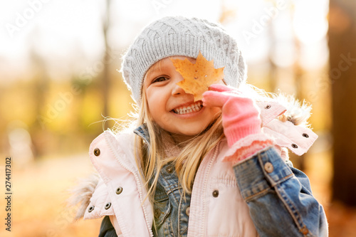 childhood  season and people concept - happy little girl with maple leaf at autumn park