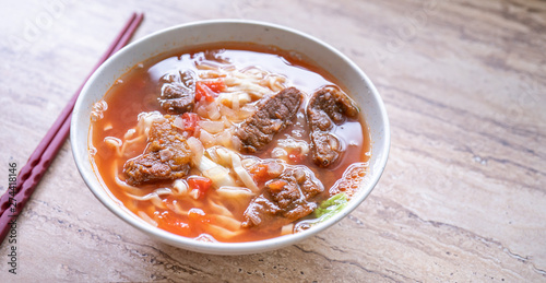 Beef noodle ramen meal with tomato sauce broth in bowl on bright wooden table, famous chinese style food in Taiwan, close up, top view, copy space