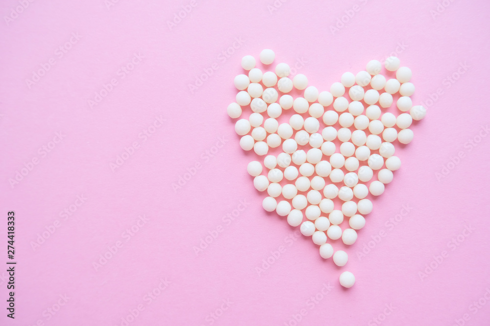 Heart made of homeopathic globules on pink background. Alternative Homeopathy medicine herbs, healtcare and pills concept. Flatlay. Top view. copyspace for text Heart made of homeopathic globules on pink background. Alternative Homeopathy medicine herbs, healtcare and pills concept. Flatlay. Top view. copyspace for text