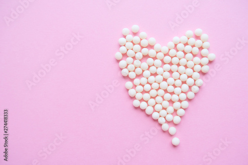 Heart made of homeopathic globules on pink background. Alternative Homeopathy medicine herbs, healtcare and pills concept. Flatlay. Top view. copyspace for text