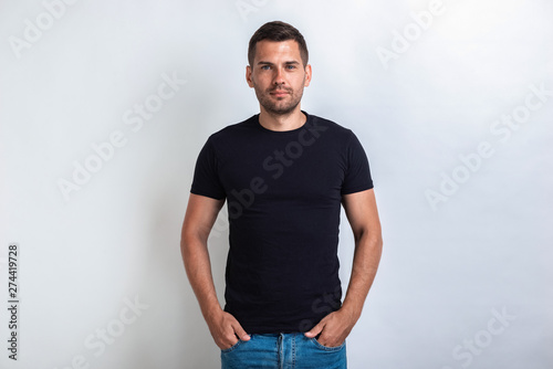 Nice man wearing in black t-shirt standing holding his arms in pocket, seriously looking at the camera