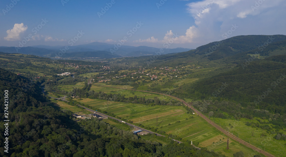 Aerial view of the Carpathian mountains. Natural background with geometric pattern - beige and red rectangles of the fields and roofs and lines of roads and trees. Zakarpattia, Ukraine.