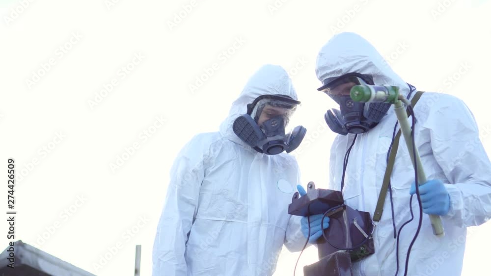 two scientists in protective suits and masks and make measurements of radiation against the background of the ruins at sunset two scientists in protective suits and masks and make measurements of radiation against the background of the ruins at sunset