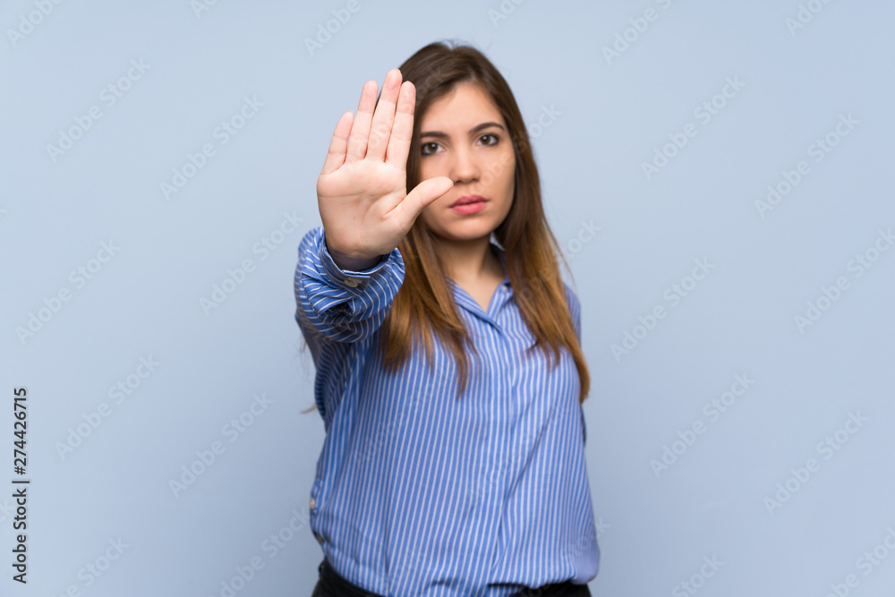 Young girl over isolated blue wall making stop gesture Young girl over isolated blue wall making stop gesture