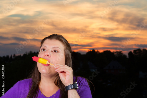 Woman portrait eating an ice-cream Popsicle during a summer sunset