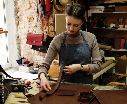 Bild auf Leinwand young woman works in a bag making studio, cuts out details