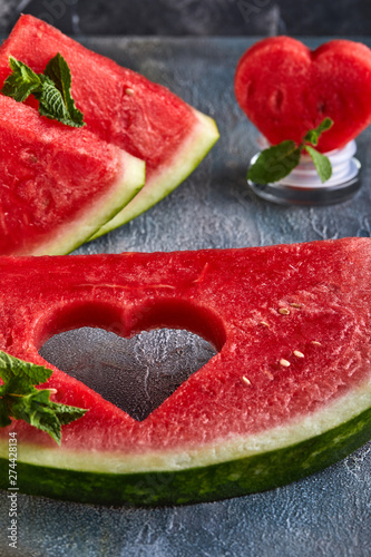 Composition with ripe watermelon, mint leaves and a heart carved in a slice of watermelon, on a background with a blue tint. Concept for valentines day