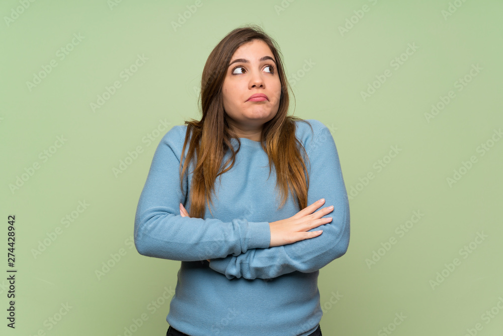 Young girl over green wall making doubts gesture while lifting the shoulders Young girl over green wall making doubts gesture while lifting the shoulders