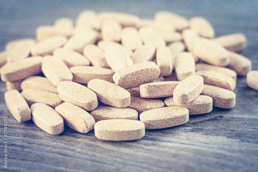 A pile of vegetable-based pills as a dietary supplement on a wooden table A pile of vegetable-based pills as a dietary supplement on a wooden table