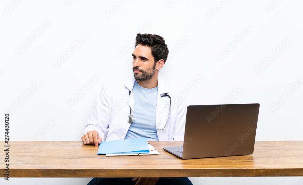 Young doctor man with his laptop over isolated wall looking side Young doctor man with his laptop over isolated wall looking side