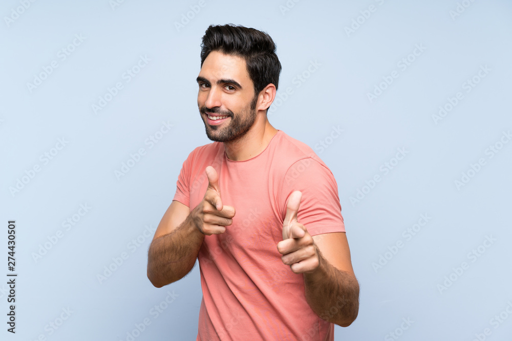 Handsome young man in pink shirt over isolated blue background pointing to the front and smiling Handsome young man in pink shirt over isolated blue background pointing to the front and smiling