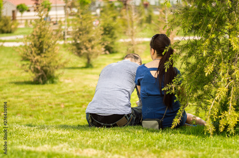 Back side of a young couple sitting on grass in a park on a sunny day