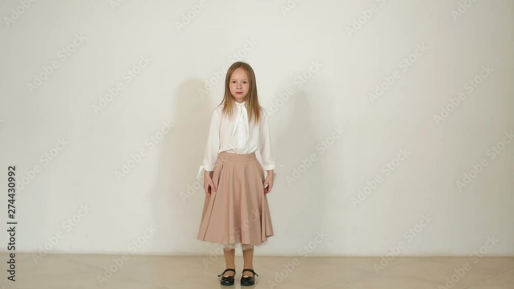 A cute little girl in a white blouse and a long skirt jumps and has fun on a white background, her skirt flies in different directions. Slow motion.