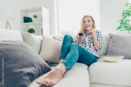 Low angle view of her she nice-looking attractive lovely charming cute cheerful cheery glad wavy-haired girl in checked shirt lying on divan looking comedian at white light style interior living-room