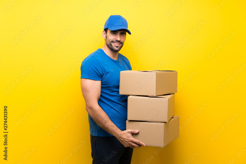 Young delivery man over isolated yellow wall Young delivery man over isolated yellow wall
