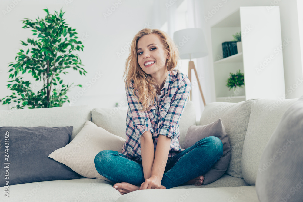 Portrait of her she nice-looking attractive lovely sweet lovable modest shine cheerful cheery wavy-haired girl in checked shirt sitting on divan having fun at white light style interior living-room