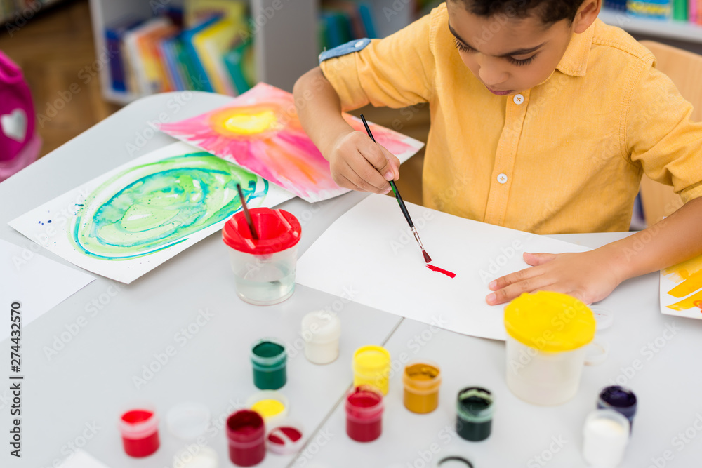 selective focus of african american kid painting while holding paintbrush