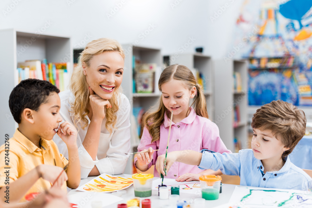 selective focus of happy woman looking at camera near cute kids