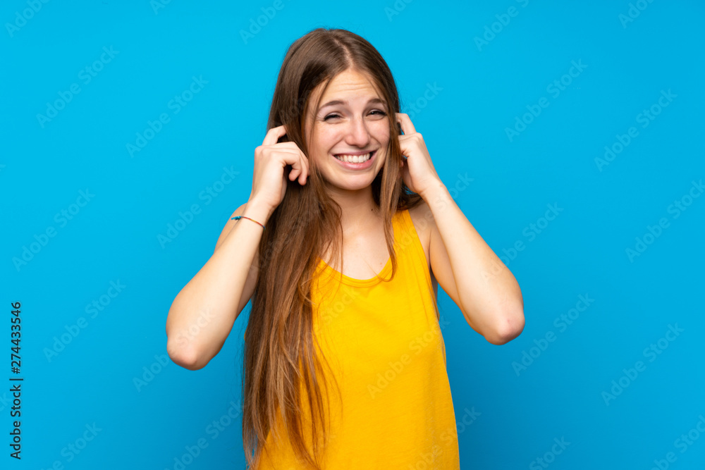 Young woman with long hair over isolated blue wall frustrated and covering ears Young woman with long hair over isolated blue wall frustrated and covering ears
