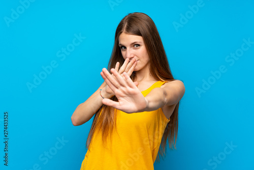 Young woman with long hair over isolated blue wall nervous stretching hands to the front