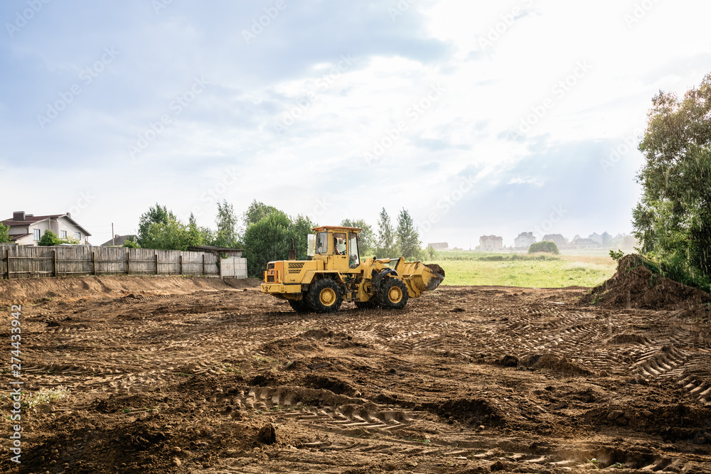 Fototapeta large yellow wheel loader aligns a piece of land for a new building
