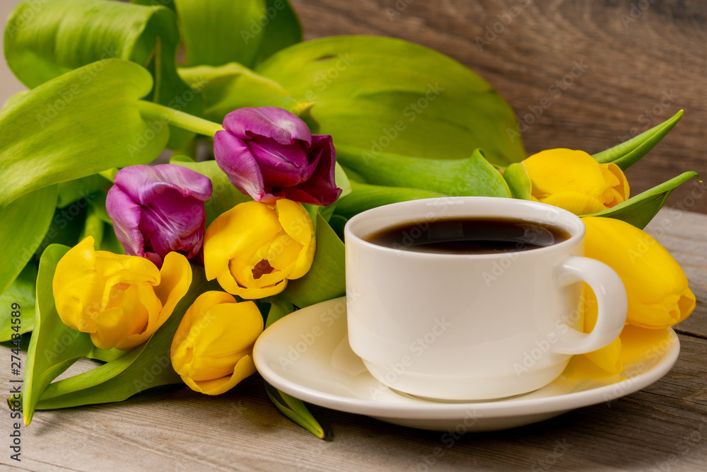 Obraz premium Yellow and purple tulips and coffee cup on rustic wooden table. Close up shot.