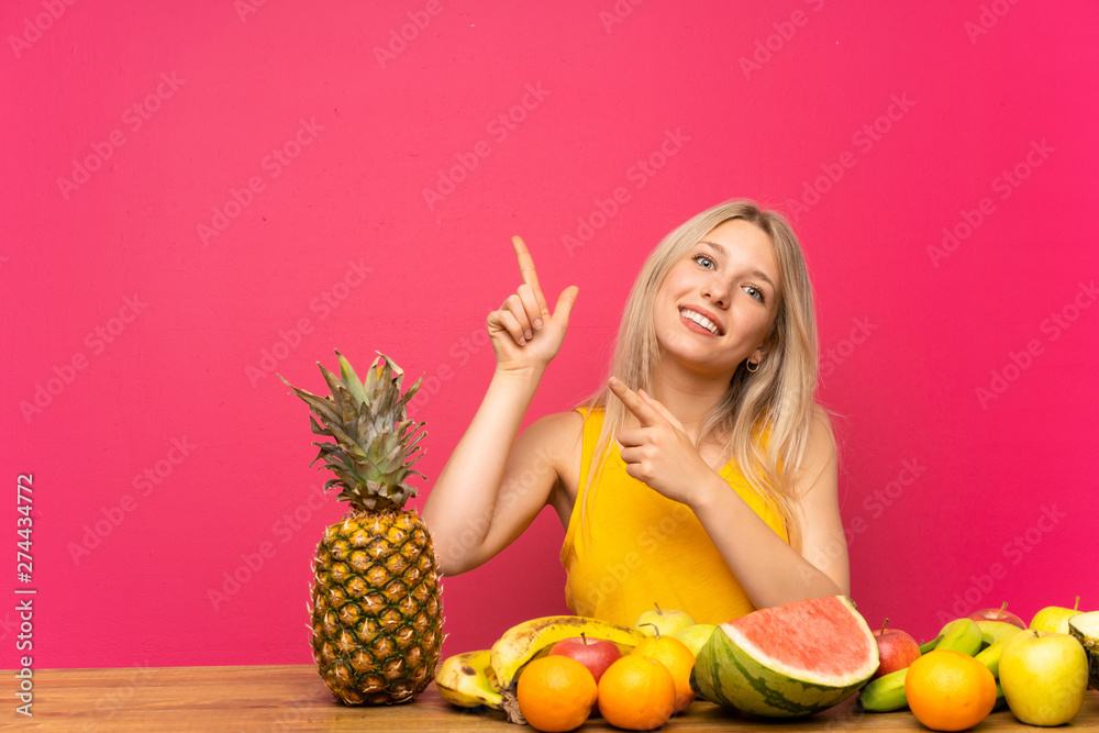 Young blonde woman with lots of fruits pointing with the index finger a great idea Young blonde woman with lots of fruits pointing with the index finger a great idea