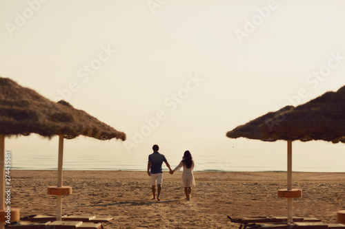 Couple in love having romantic tender moments on the beach near wicker umbrellas. Young lovers enjoying summer vacation