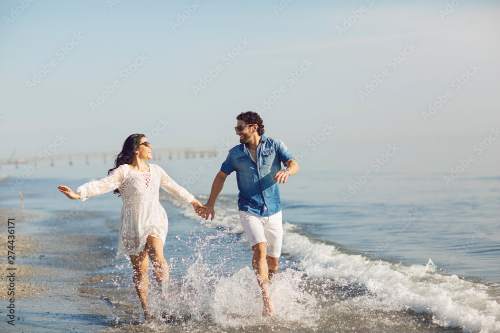 Happy couple walking and playing on the beach, soaking his feet in the water. Wonderful love story in Rimini, Italy