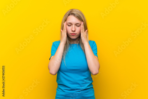 Young blonde woman over isolated yellow background with headache