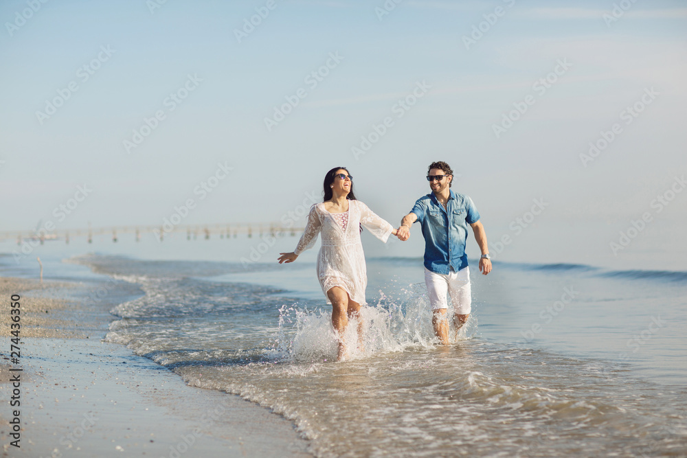 Happy couple walking and playing on the beach, soaking his feet in the water. Wonderful love story in Rimini, Italy Happy couple walking and playing on the beach, soaking his feet in the water. Wonderful love story in Rimini, Italy