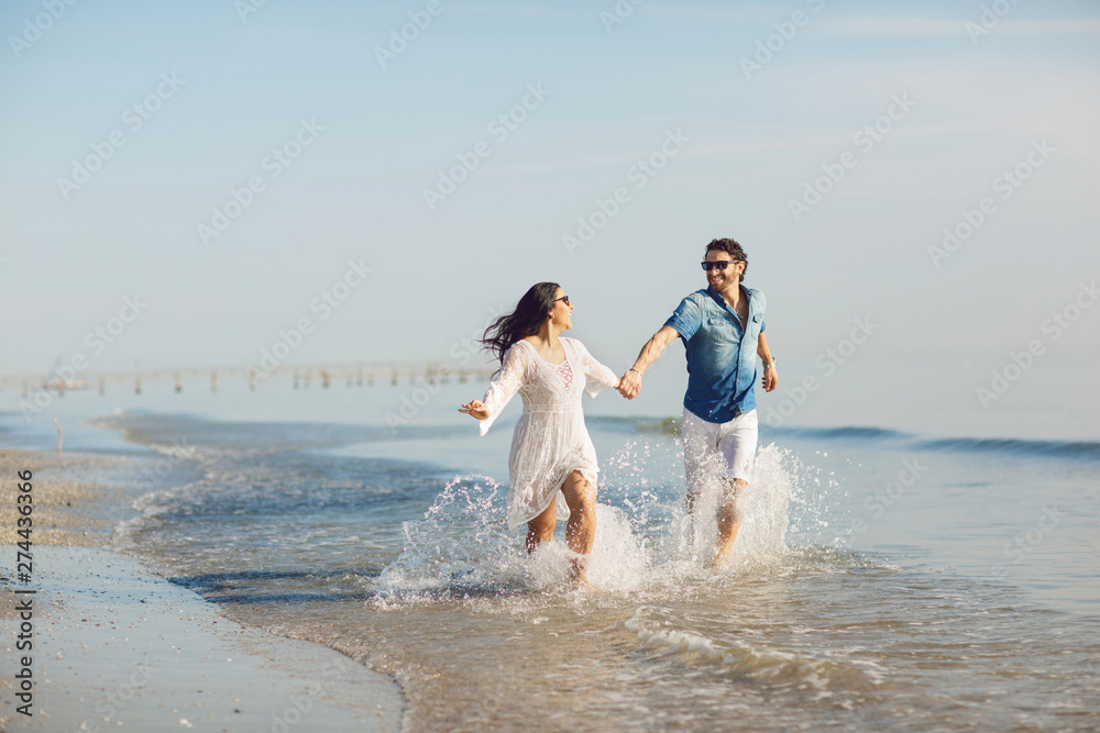 Happy couple walking and playing on the beach, soaking his feet in the water. Wonderful love story in Rimini, Italy Happy couple walking and playing on the beach, soaking his feet in the water. Wonderful love story in Rimini, Italy