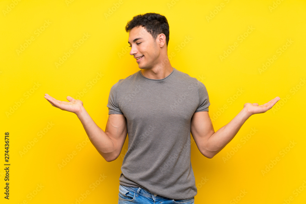 Handsome man over isolated yellow wall holding copyspace with two hands Handsome man over isolated yellow wall holding copyspace with two hands