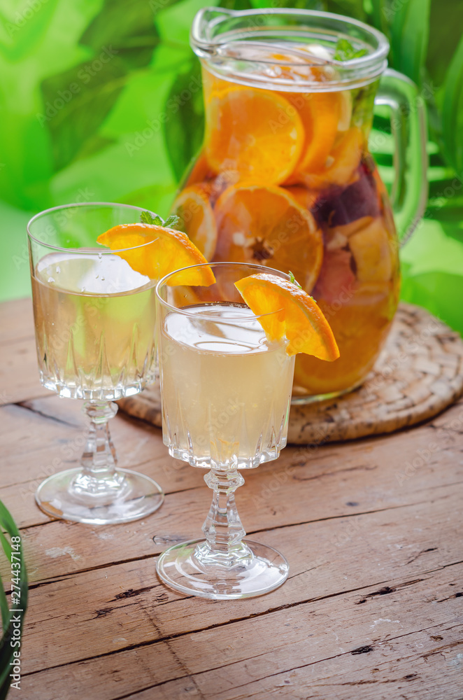 Glass of white sparkling wine sangria decorated with citrus slices and season fruits on wooden table.