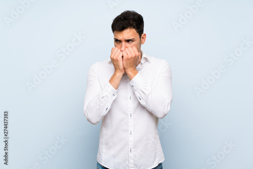 Handsome man over blue wall nervous and scared putting hands to mouth