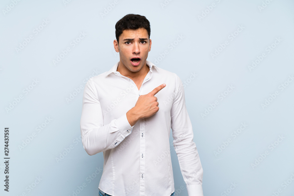 Handsome man over blue wall surprised and pointing side Handsome man over blue wall surprised and pointing side