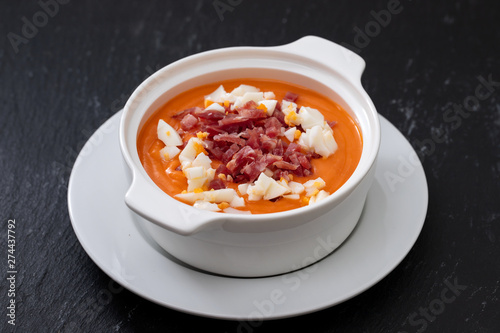 Typical Spanish soup salmorejo cream with ham and egg in white bowl on ceramic background. Top view.
