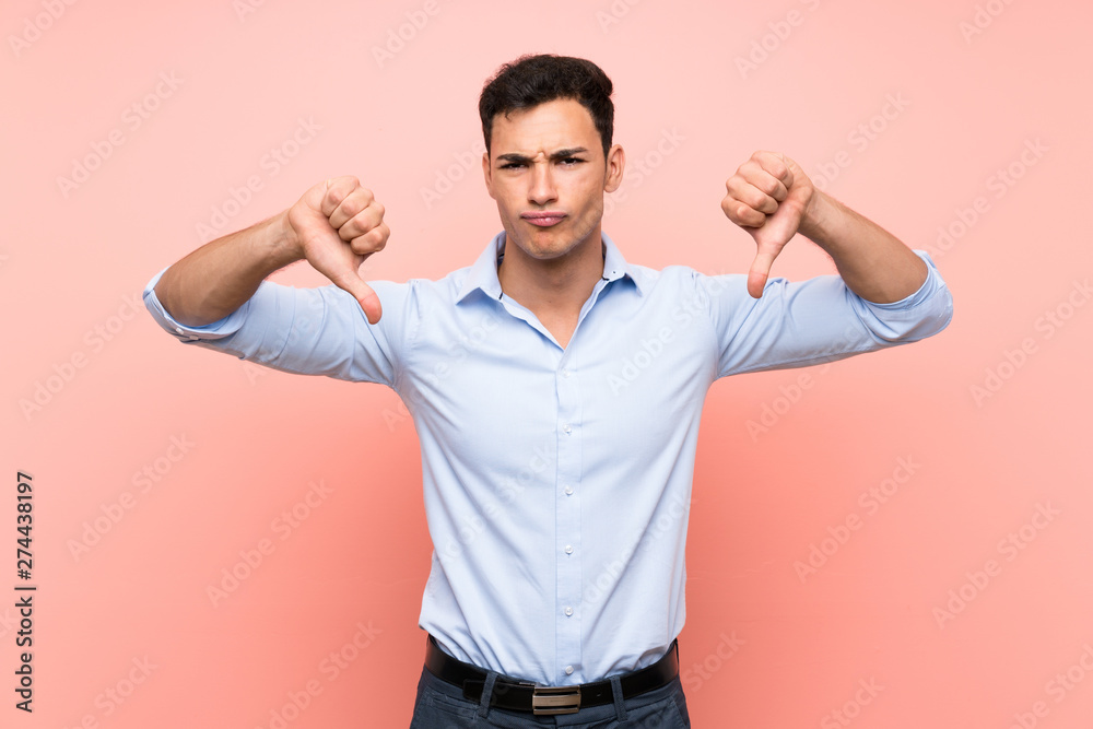 Fototapeta premium Handsome man over pink background showing thumb down