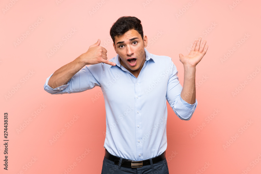 Handsome man over pink background making phone gesture and doubting Handsome man over pink background making phone gesture and doubting