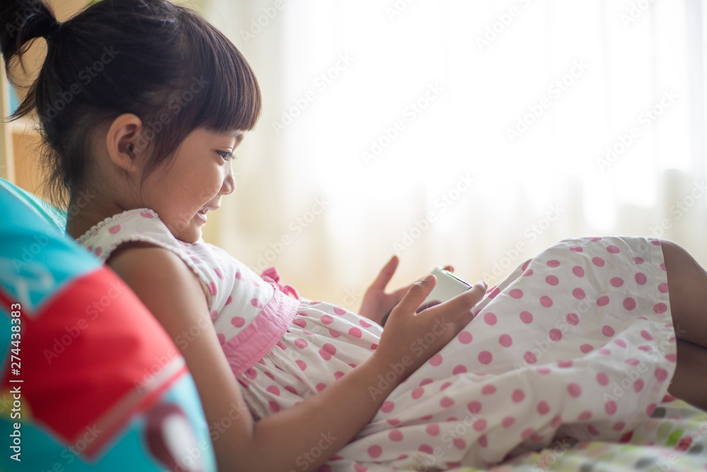 child, technology and internet concept - little girl lying in bed with smartphone at home child, technology and internet concept - little girl lying in bed with smartphone at home