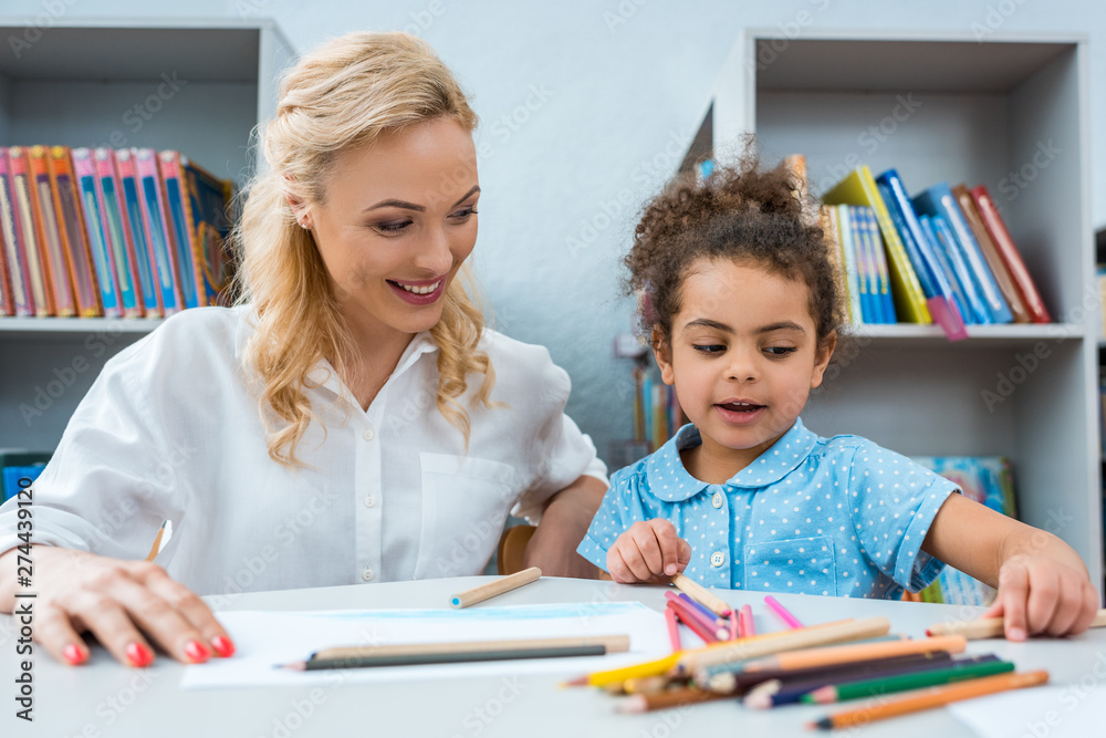 selective focus of happy woman looking at cute african american kid selective focus of happy woman looking at cute african american kid