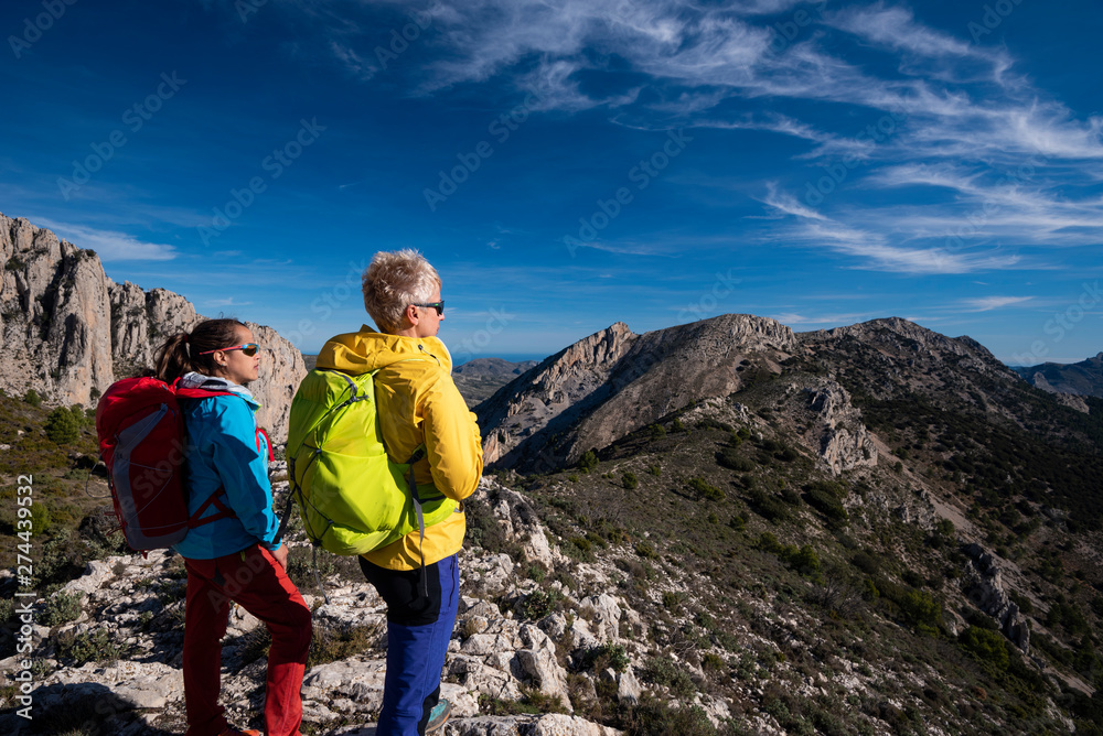 Two women on a hike looking towards the valley, hiking in Sierra de Serrella, Quatretondeta-Confrides, Alicante province, Comunidad Valenciana region, Spain