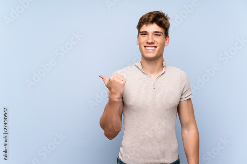 Handsome young man over isolated blue wall pointing to the side to present a product