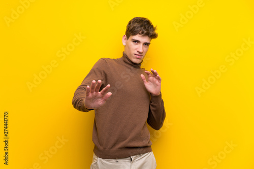 Handsome young man over isolated yellow background nervous stretching hands to the front