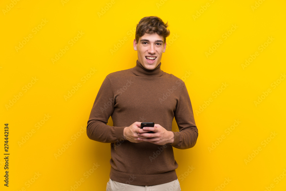 Handsome young man over isolated yellow background surprised and sending a message Handsome young man over isolated yellow background surprised and sending a message