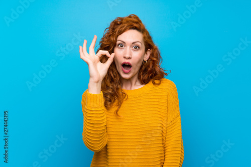 Redhead woman with yellow sweater surprised and showing ok sign