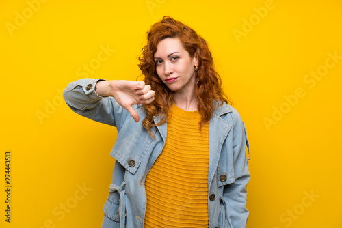 Redhead woman over isolated yellow background showing thumb down sign