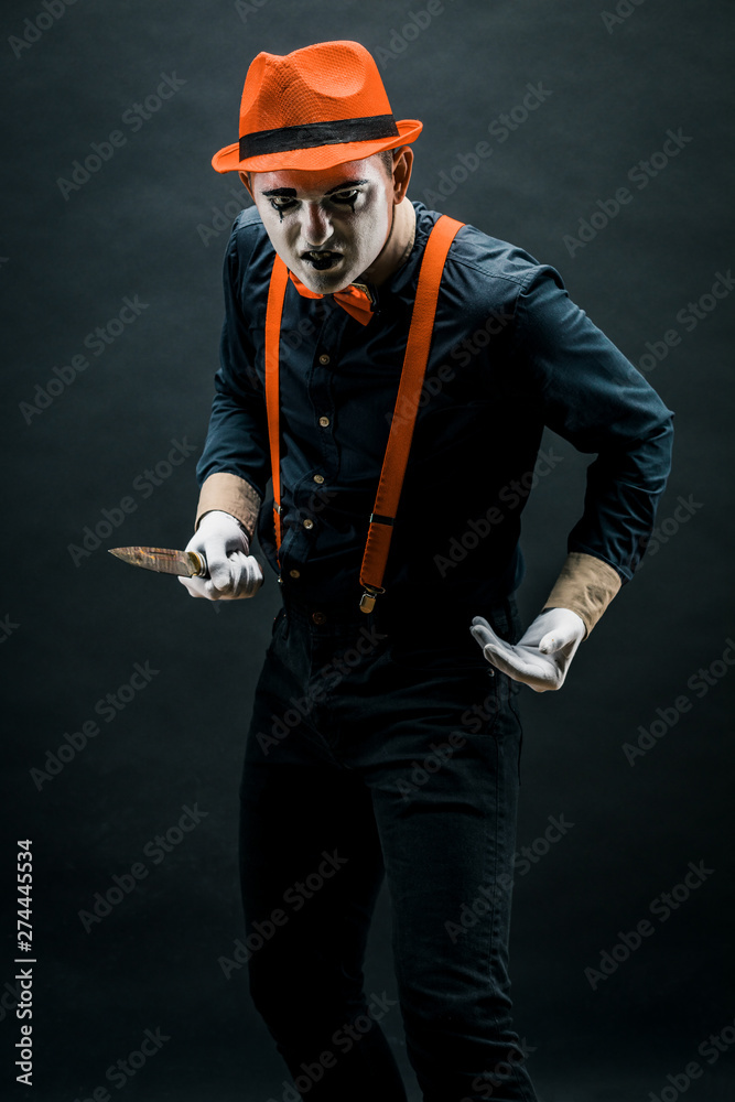 clown and Halloween theme: crazy clown with knife in hand isolated on dark background in Studio.