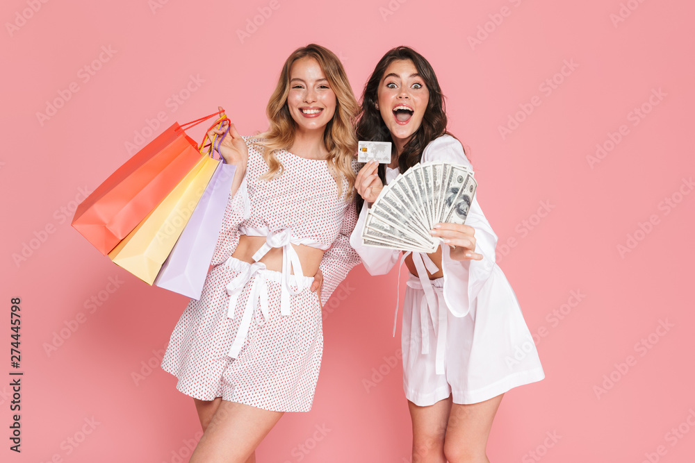 Happy young pretty women friends posing isolated over pink wall background holding shopping bags, credit card and money. Happy young pretty women friends posing isolated over pink wall background holding shopping bags, credit card and money.